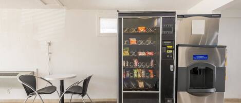 Máquina expendedora con aperitivos y dispensador de agua en una habitación con una mesa y sillas.