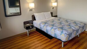 Habitación de hotel con cama, mesitas de noche, televisor montado en la pared y dos lámparas de pared.