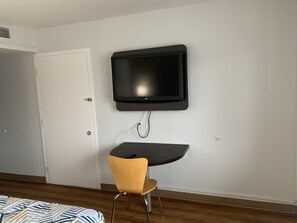 A room with a flat-screen TV mounted on the wall, a small desk with a chair, and a bed with striped bedding. - Motel 6 Dayton, OH (Dayton)