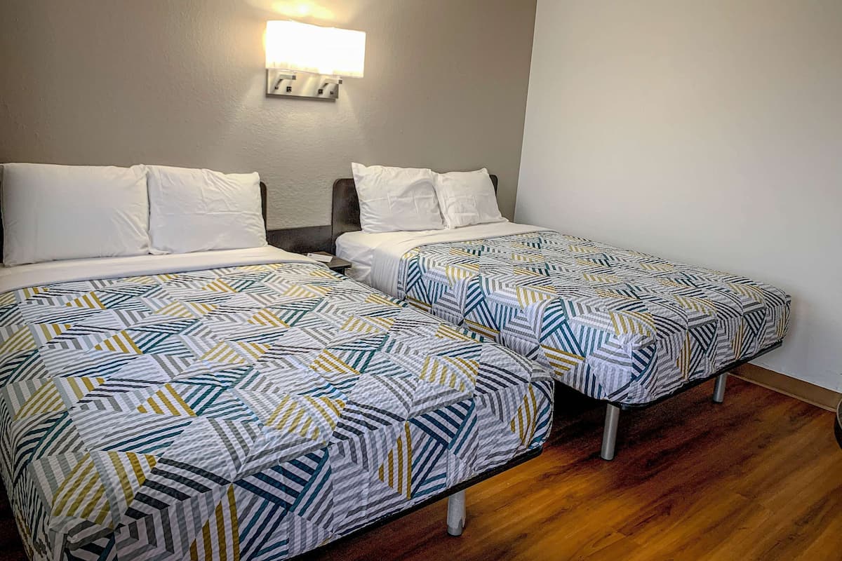 Ein Hotelzimmer mit zwei Betten, jeweils mit einer gemusterten Tagesdecke, einem Nachttisch und einer Wandleuchte.