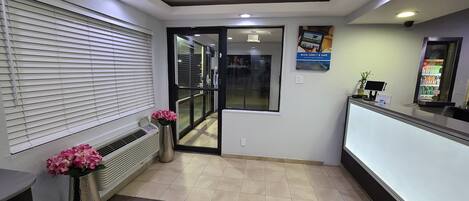 A reception area with a tiled floor, a reception desk, a potted plant, and a wall-mounted sign.