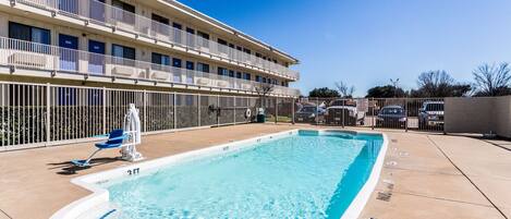 A swimming pool with a white border, a blue chair, and a building with balconies in the background.