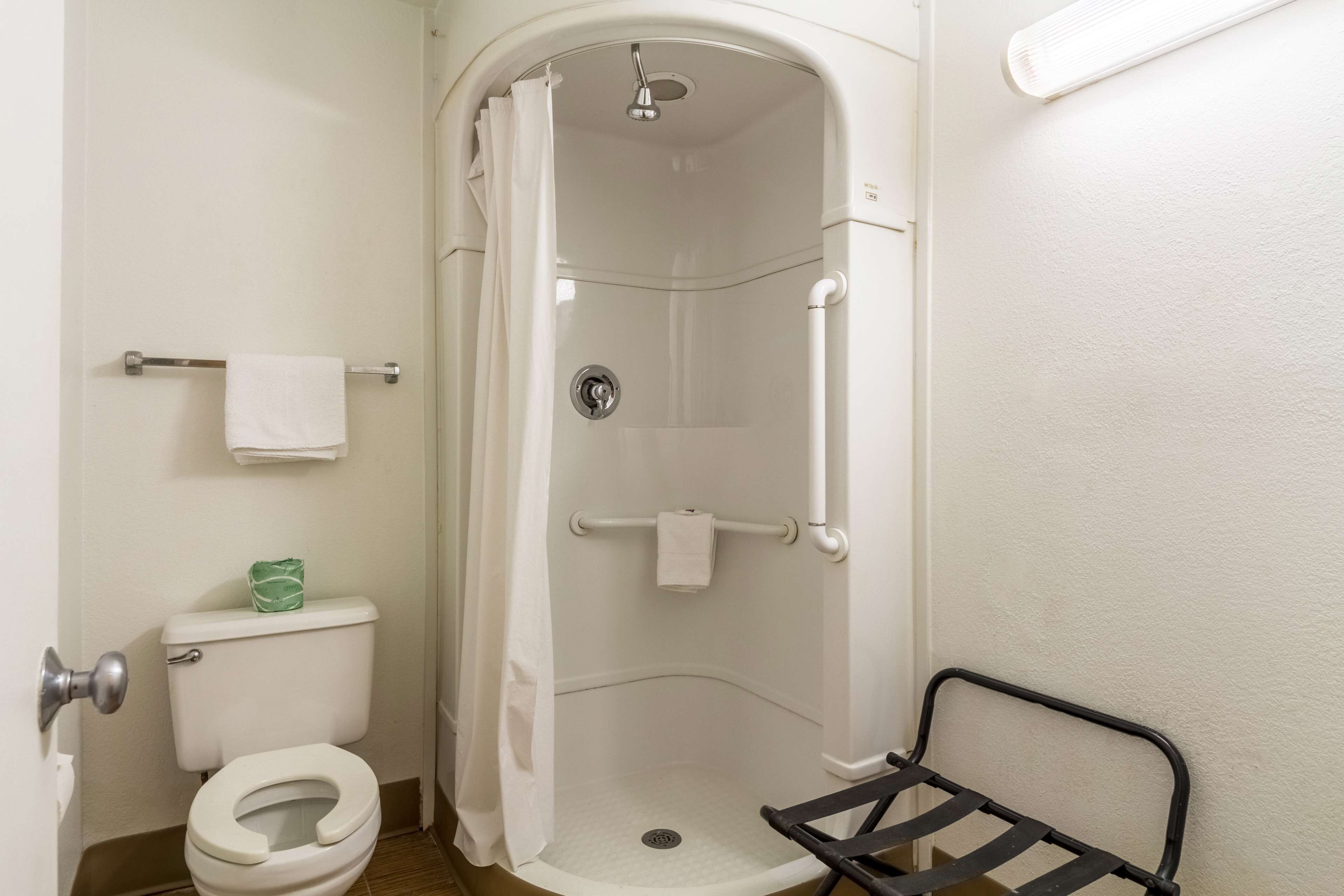 Une petite salle de bain blanche, équipée de toilettes, d’une cabine de douche et d’une étagère en métal.