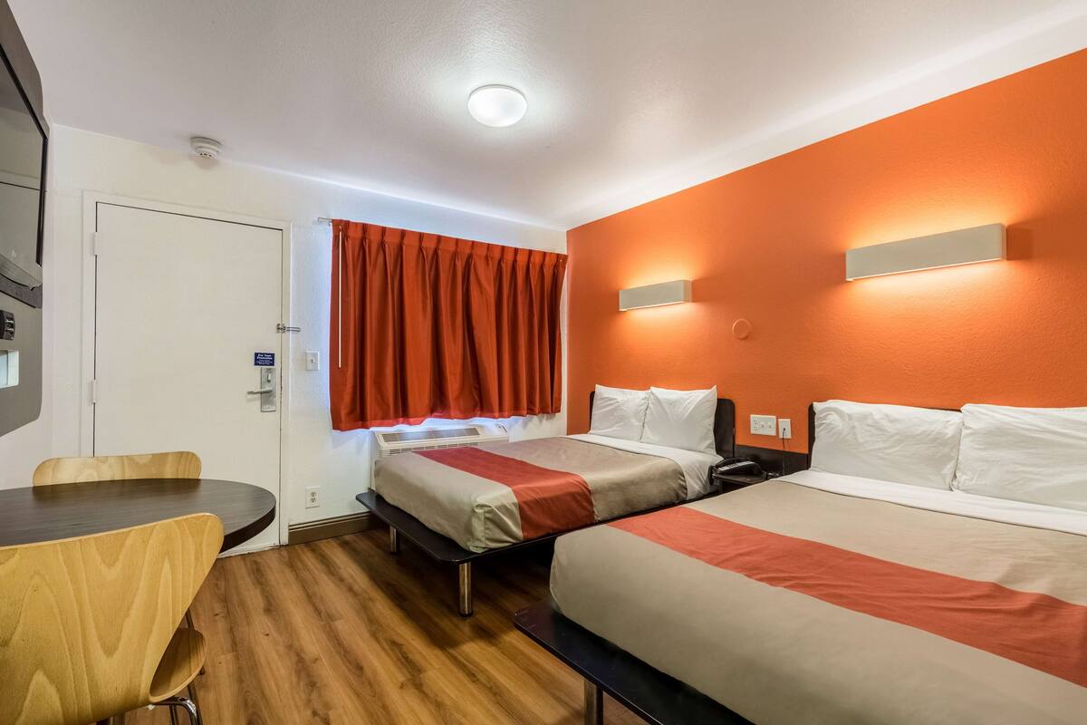 A hotel room with two beds, a desk, and a window with curtains.