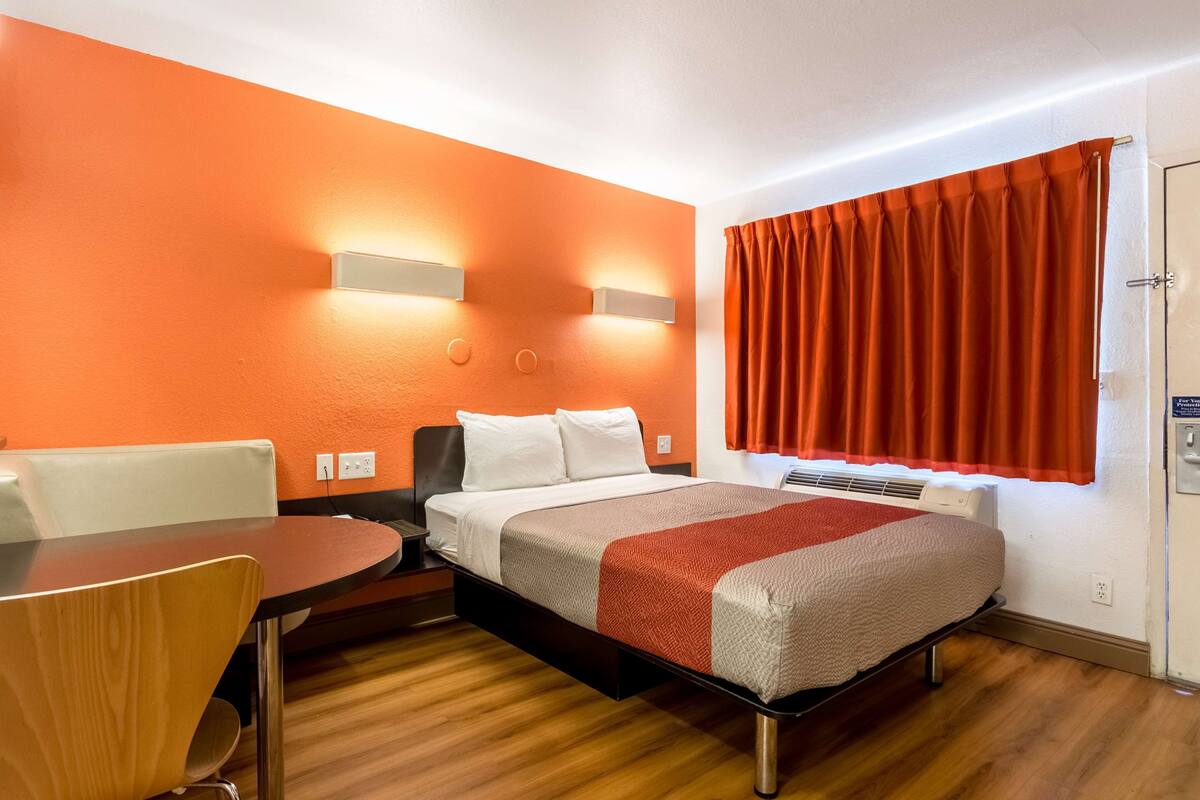 A hotel room with a bed, a desk, a chair, and a window with curtains.