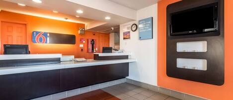 A hotel reception area with a modern design, featuring a reception desk, a clock, and a television mounted on the wall.