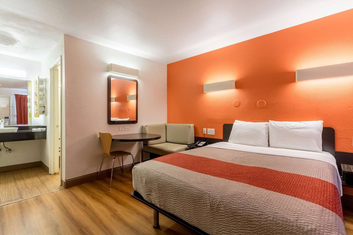 A hotel room with a bed, a desk, a chair, and a small table.