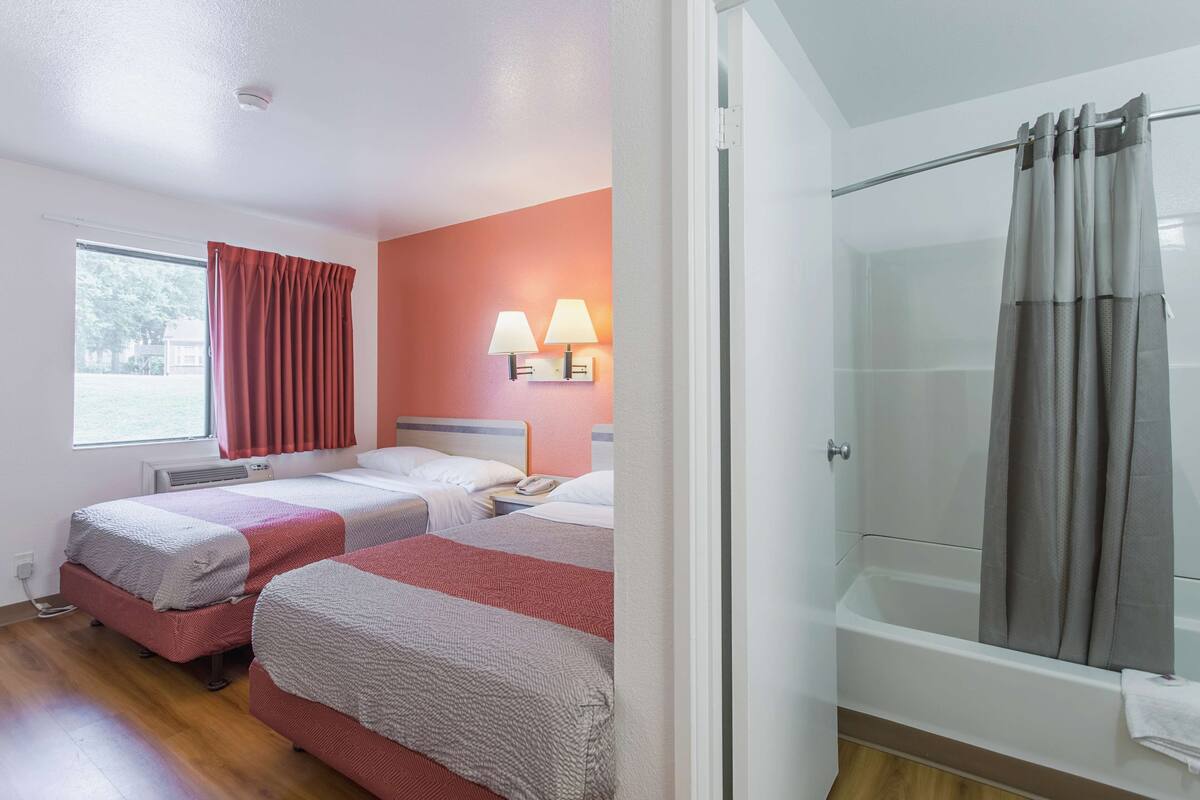 Ein Hotelzimmer mit zwei Betten, einer Dusche und einem Fenster mit Vorhängen.