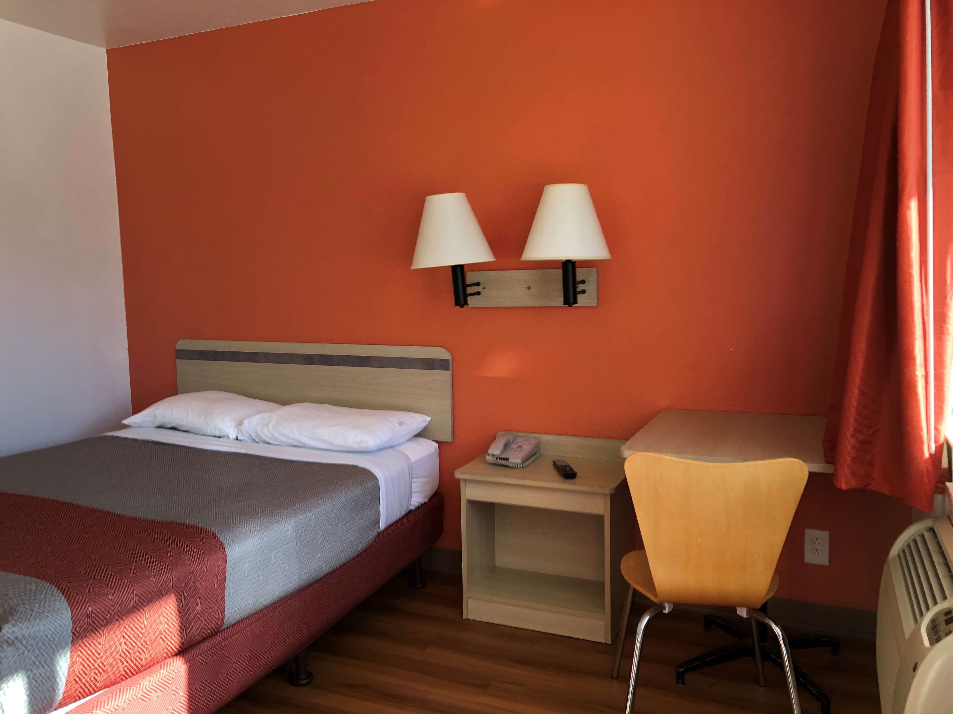 Una habitación de hotel con cama, escritorio, dos lámparas de pared y una silla.