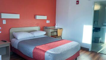 A hotel room with a bed, a desk, and a chair. There is a window and a door leading to a bathroom.