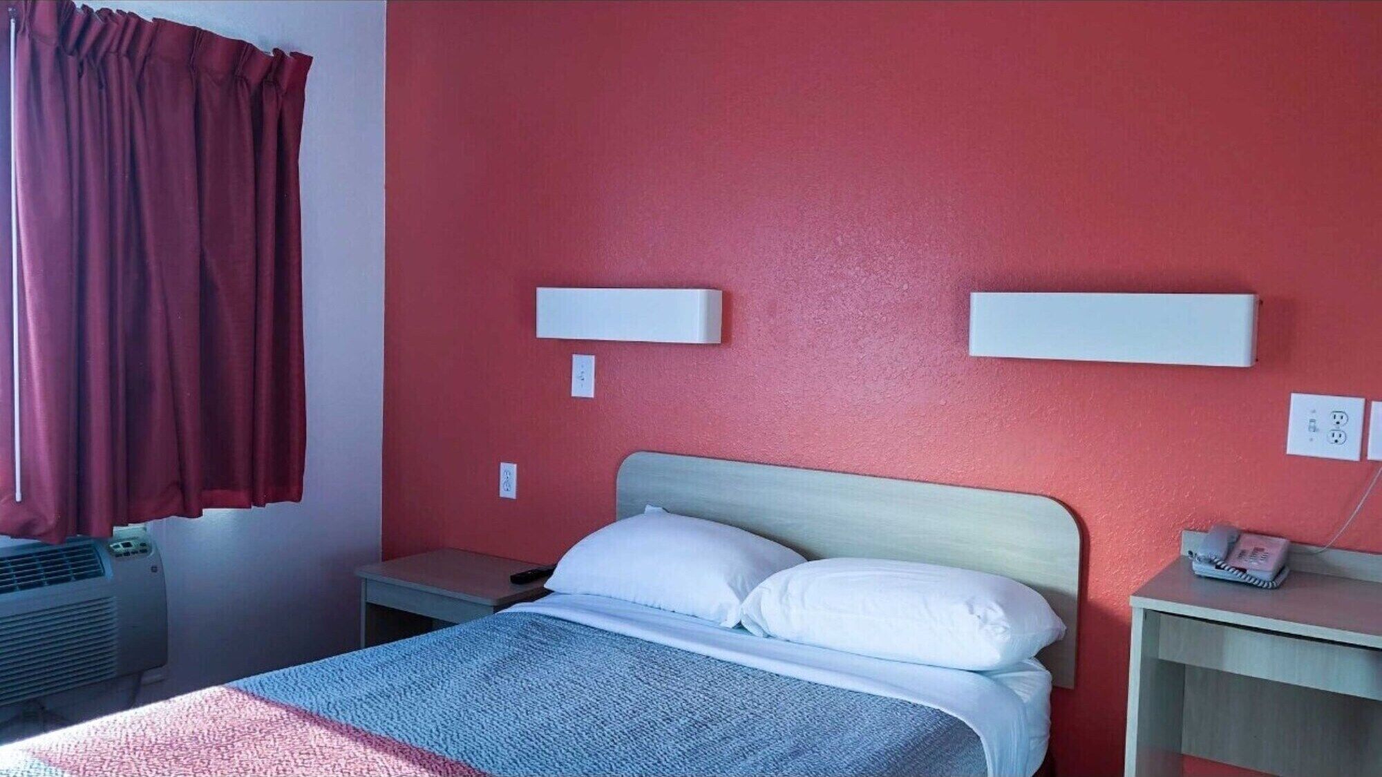 Une chambre d’hôtel équipée d’un lit, d’une table de chevet, d’un téléphone fixé au mur et d’une prise électrique.