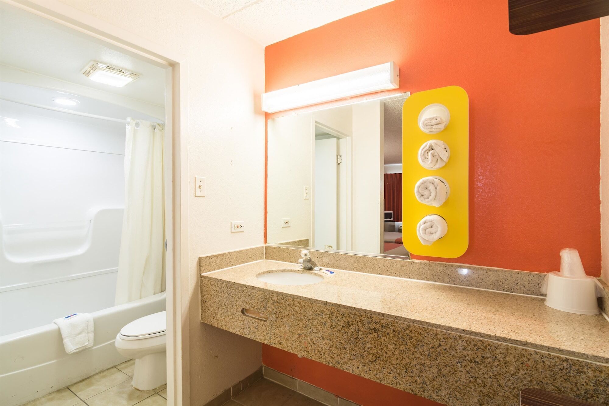 A bathroom with a white toilet, a sink with a granite countertop, and a mirror with a yellow light panel.