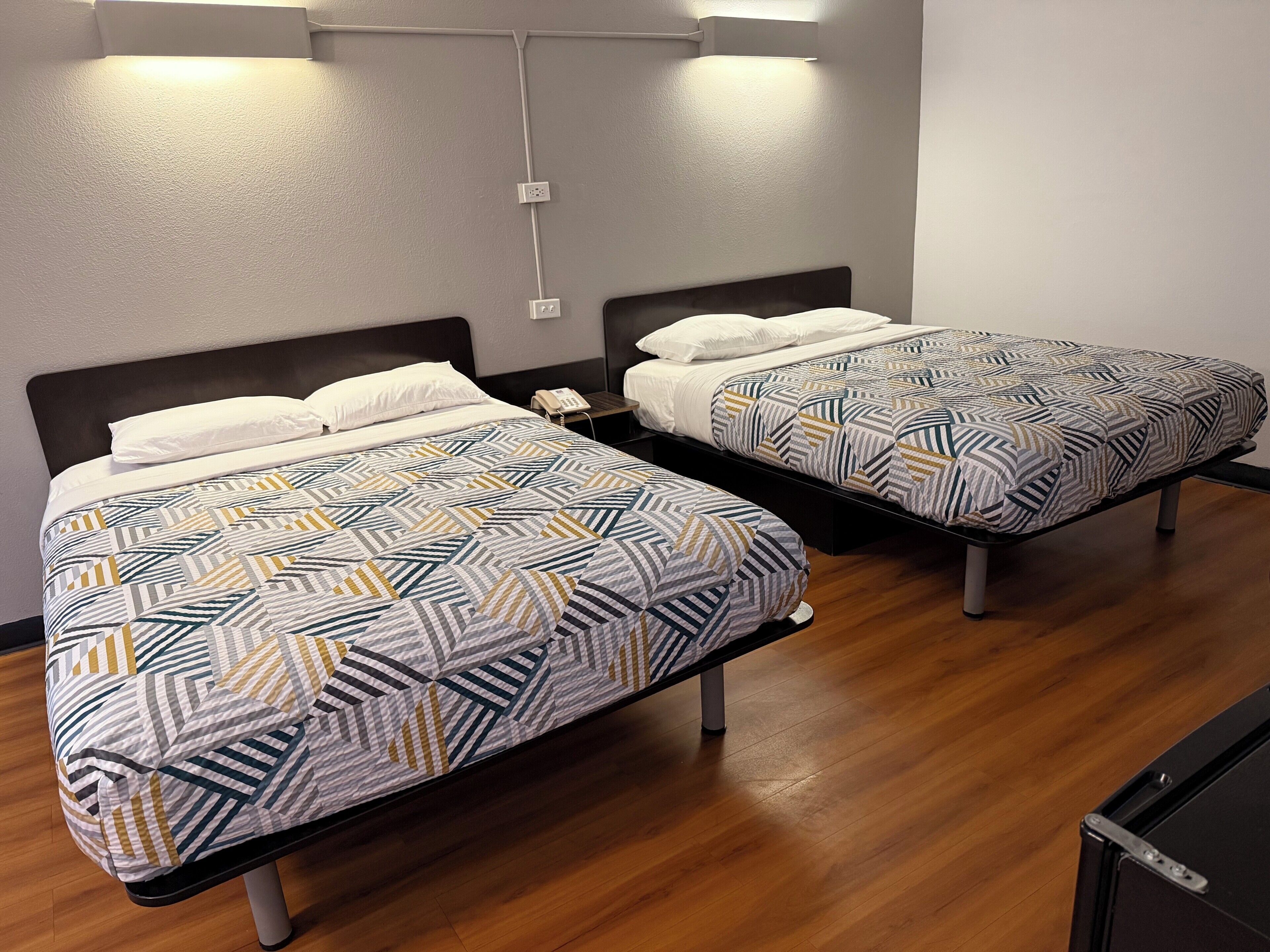 Two single beds with patterned bedding, a bedside phone, and a wall-mounted light fixture.