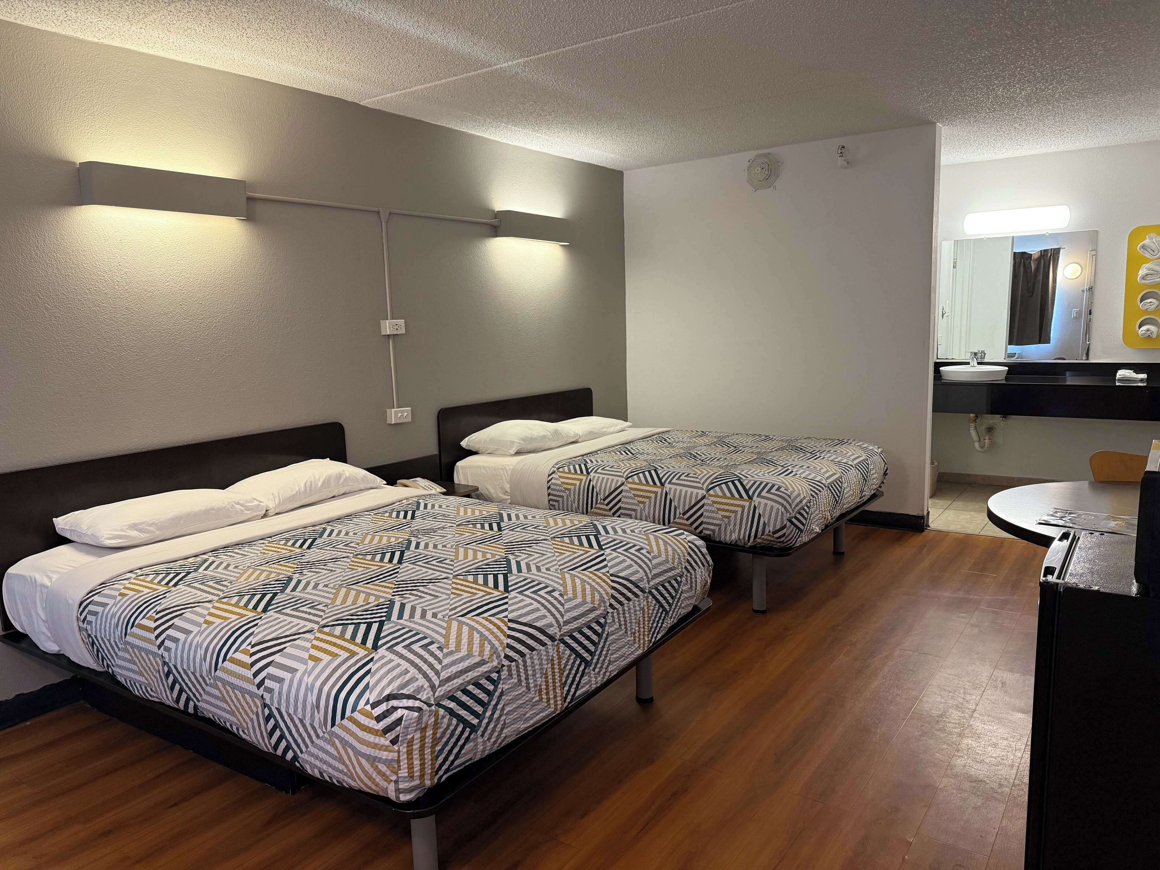 Habitación de hotel con dos camas, una mesa redonda, un lavabo y un espejo.