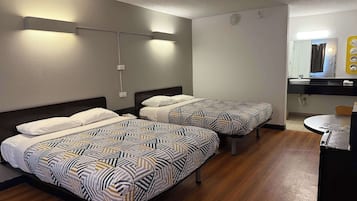 A hotel room with two beds, a round table, a sink, and a mirror.