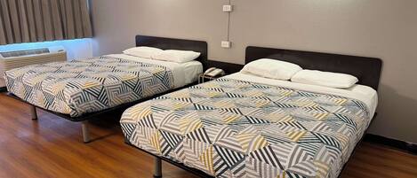 Two single beds with patterned bedding in a room with wooden flooring, a wall-mounted light, and a power outlet.