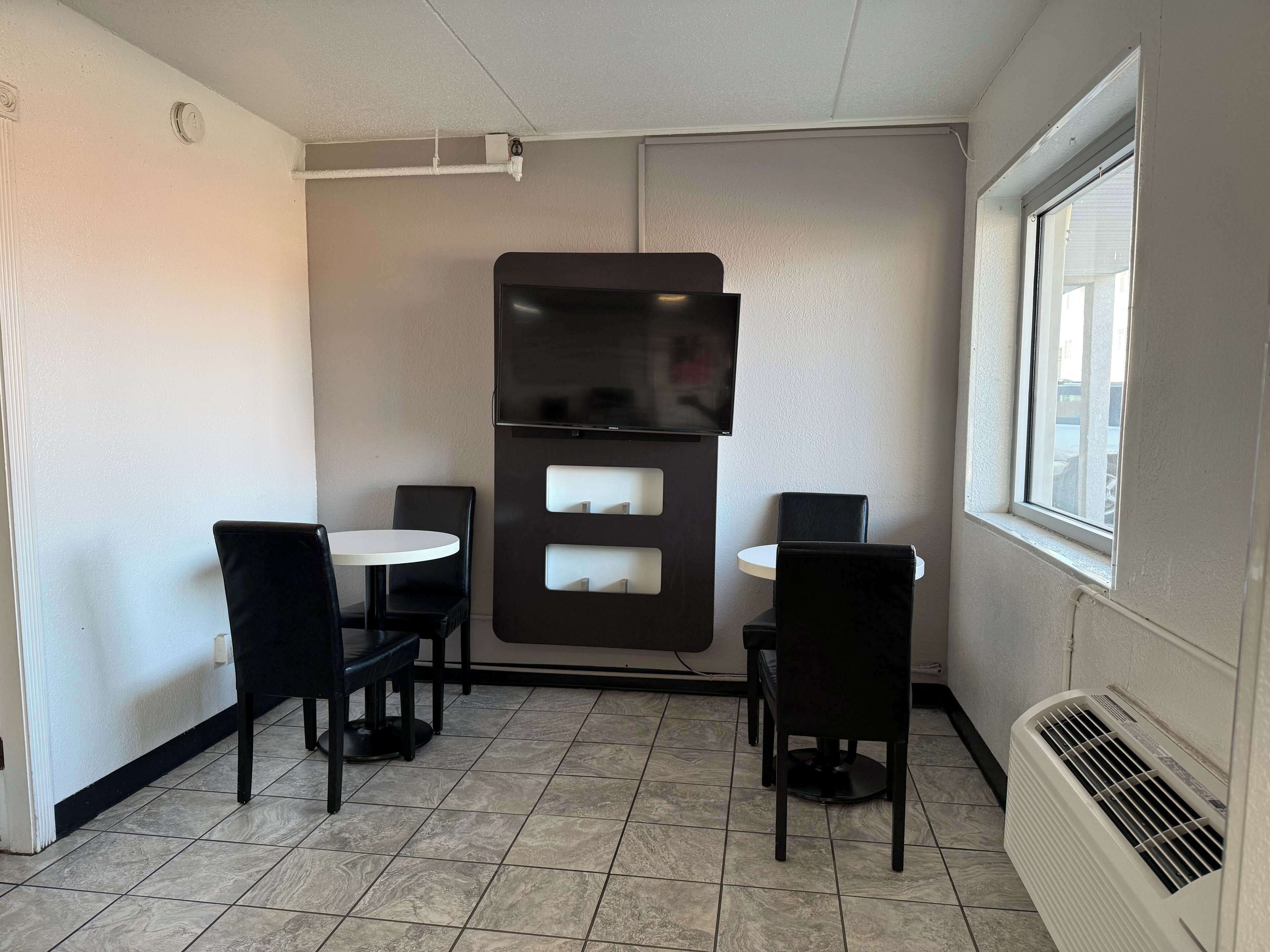 Une petite pièce privée, avec deux chaises noires et une table blanche, un téléviseur à écran plat fixé au mur et une fenêtre avec des stores.