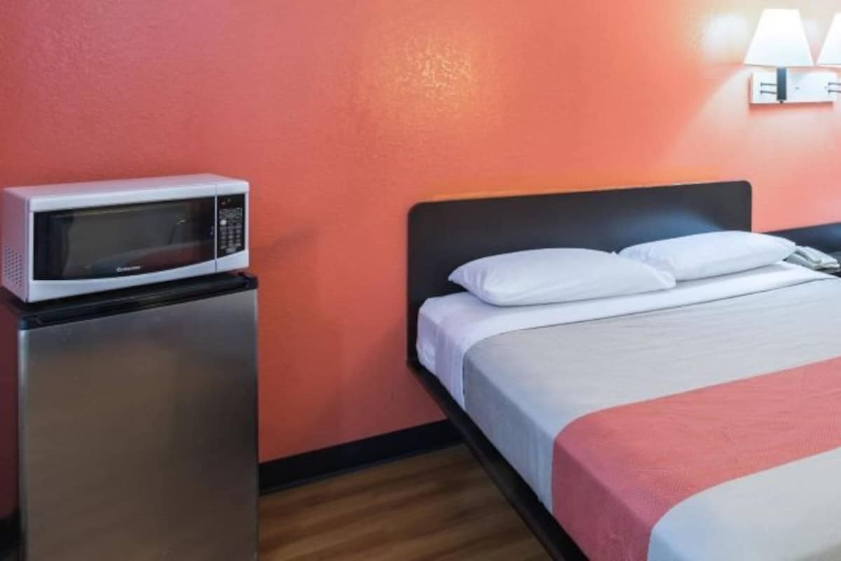 A hotel room with a bed, a microwave, and a nightstand.