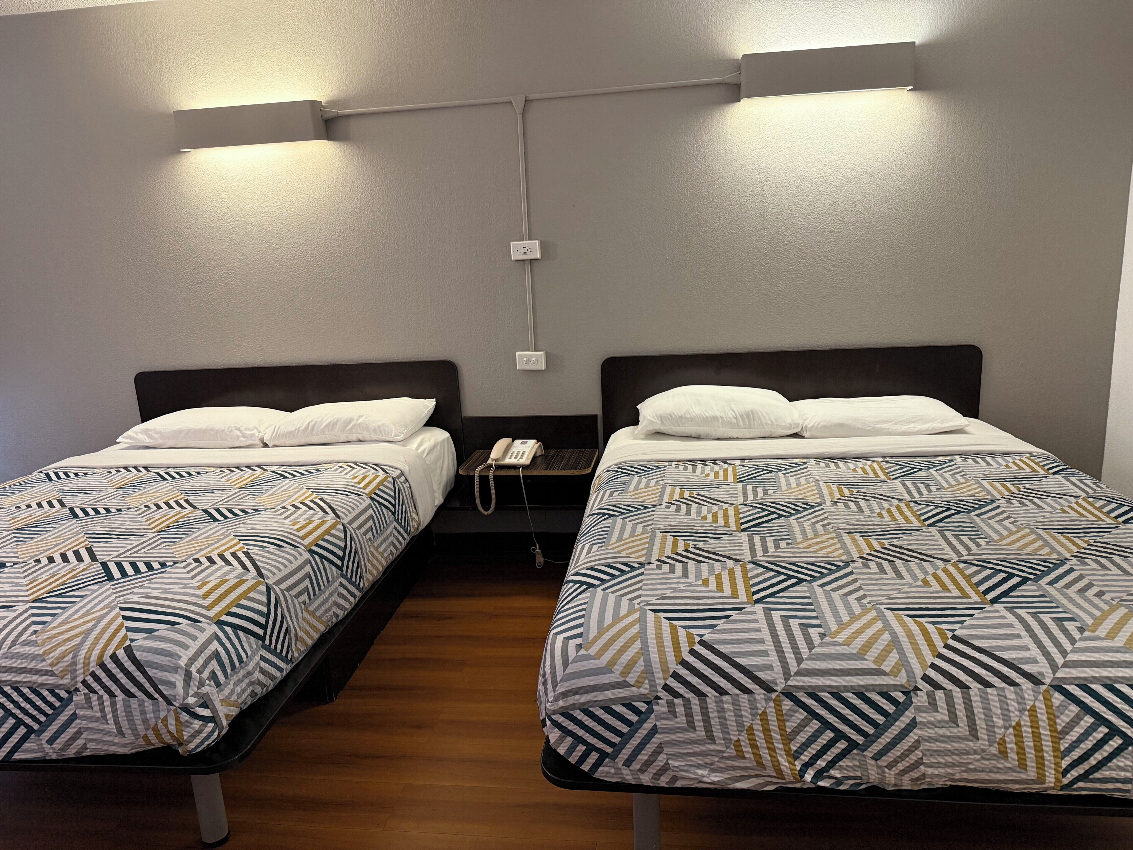 Two single beds with patterned bedding, a bedside phone, and a wall socket.