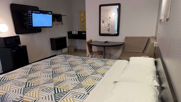 Une chambre d’hôtel équipée d’un lit, d’un bureau, d’une chaise, d’un téléviseur fixé au mur et d’un petit réfrigérateur.