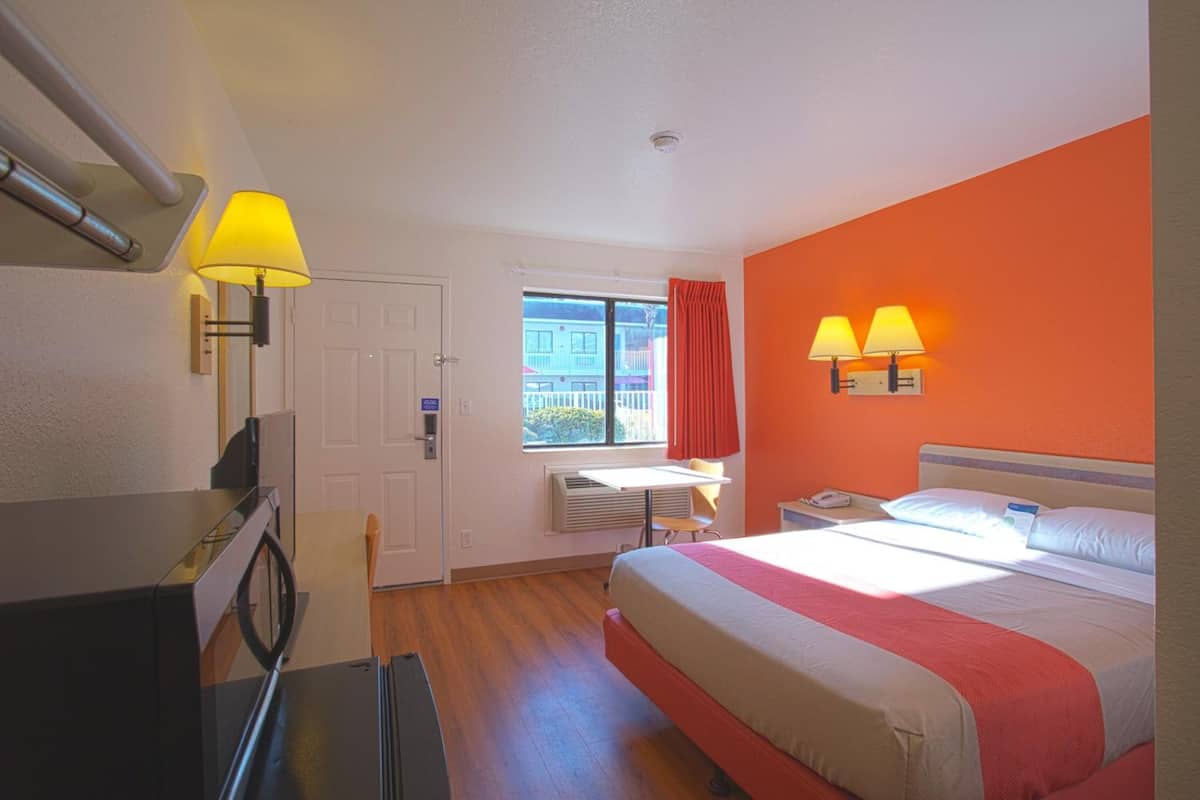 Een hotelkamer met een bed, bureau en raam met gordijnen.
