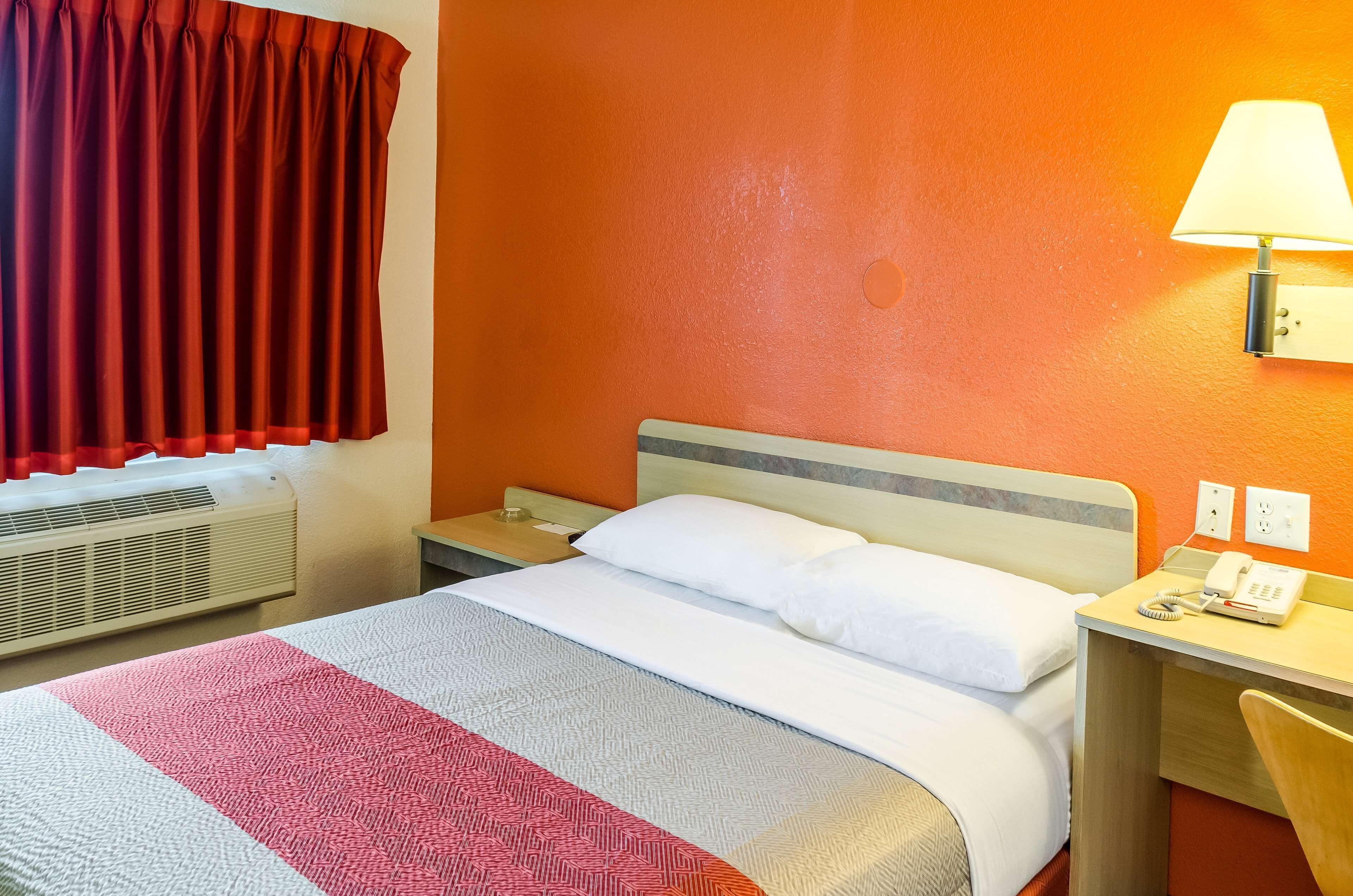 A hotel room with a bed, a desk, a lamp, and a telephone.