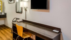 Habitación de hotel con escritorio, silla, espejo, lámpara y televisor de pantalla plana montado en la pared.