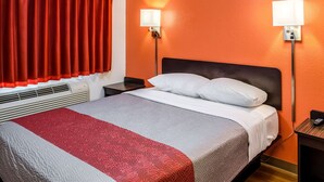 Habitación de hotel con cama, dos lámparas de noche, una mesita de noche y una ventana con cortinas rojas.