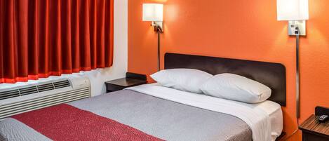 Une chambre d’hôtel avec un lit, deux lampes de chevet, une table de nuit et une fenêtre avec des rideaux rouges.