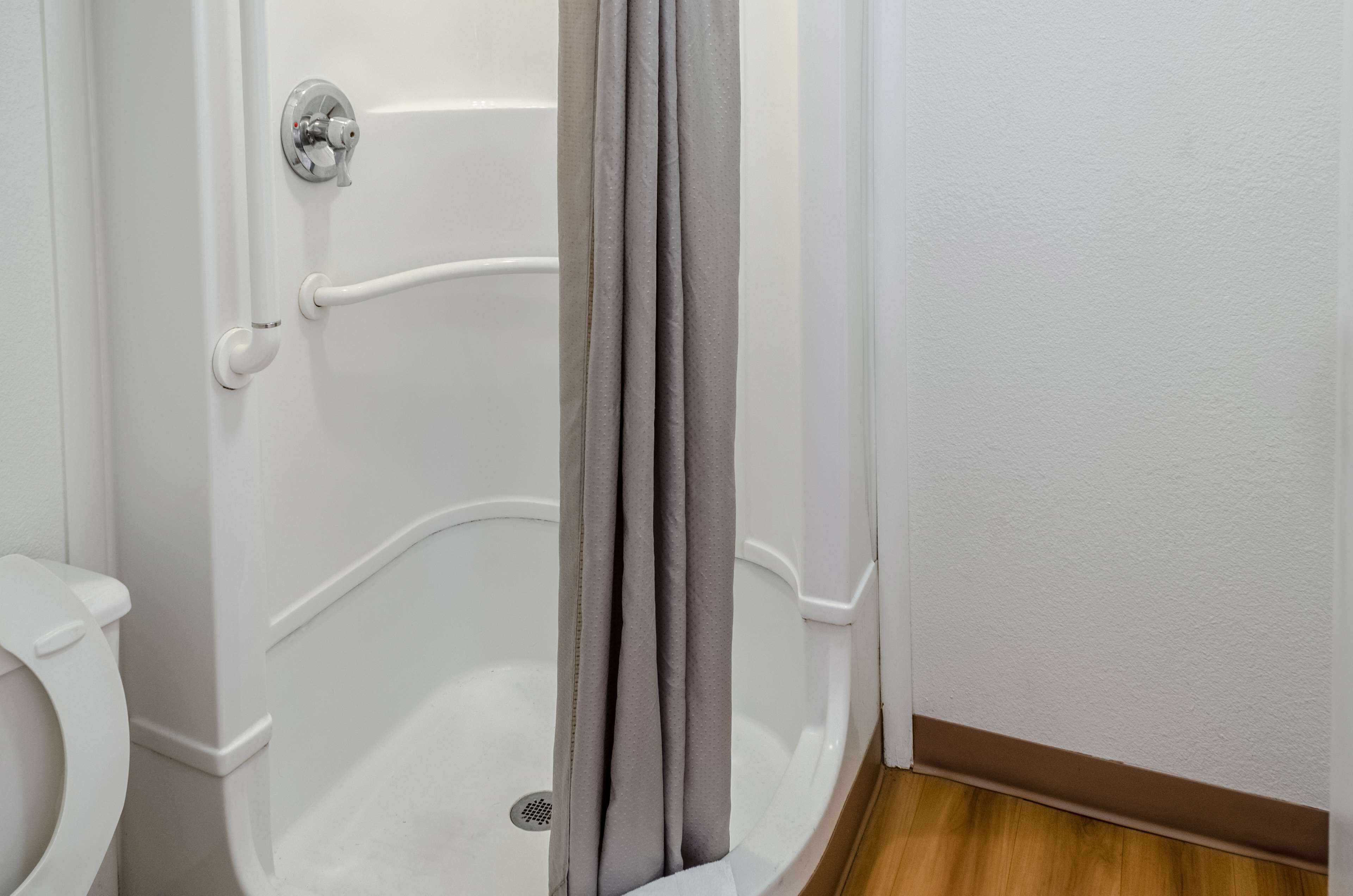 Un baño con una bañera blanca, un inodoro y una cortina de ducha gris.