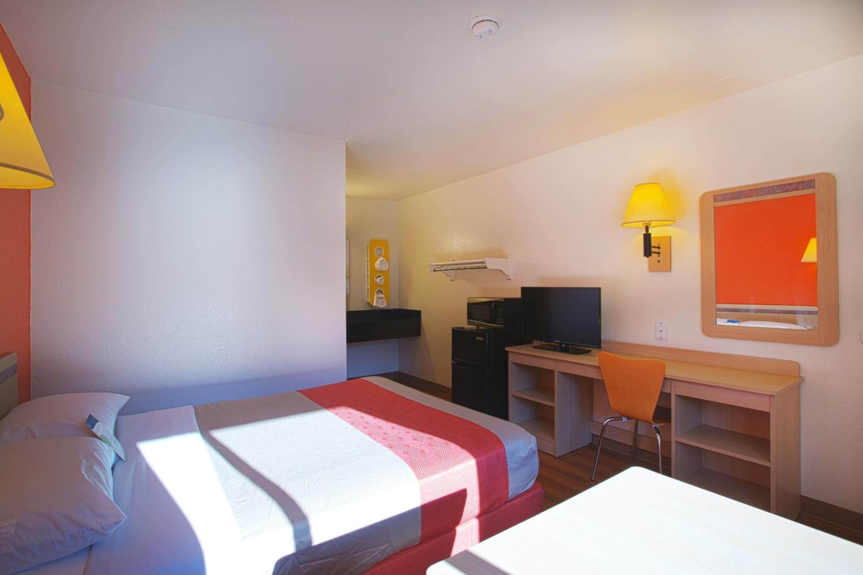 Habitación de hotel con cama, escritorio, computadora, silla y televisor.