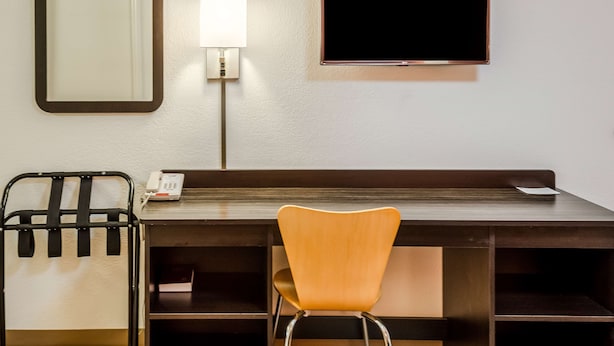 Una habitación de hotel con escritorio, silla, teléfono y televisor montado en la pared.