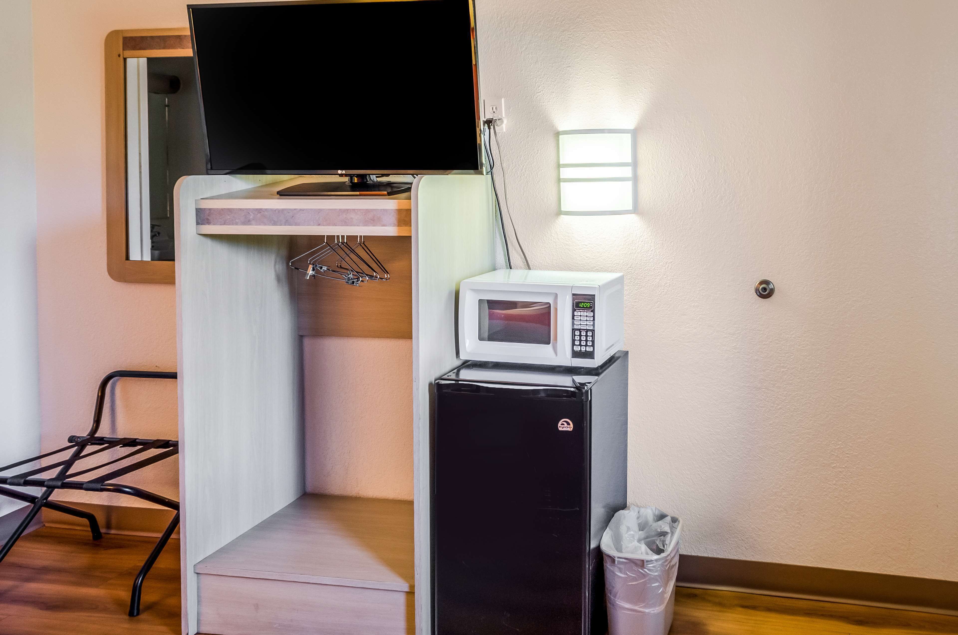 Habitació compacta amb televisió de pantalla plana penjada a la paret, microones sobre un refrigerador negre petit i un cubell de brossa.