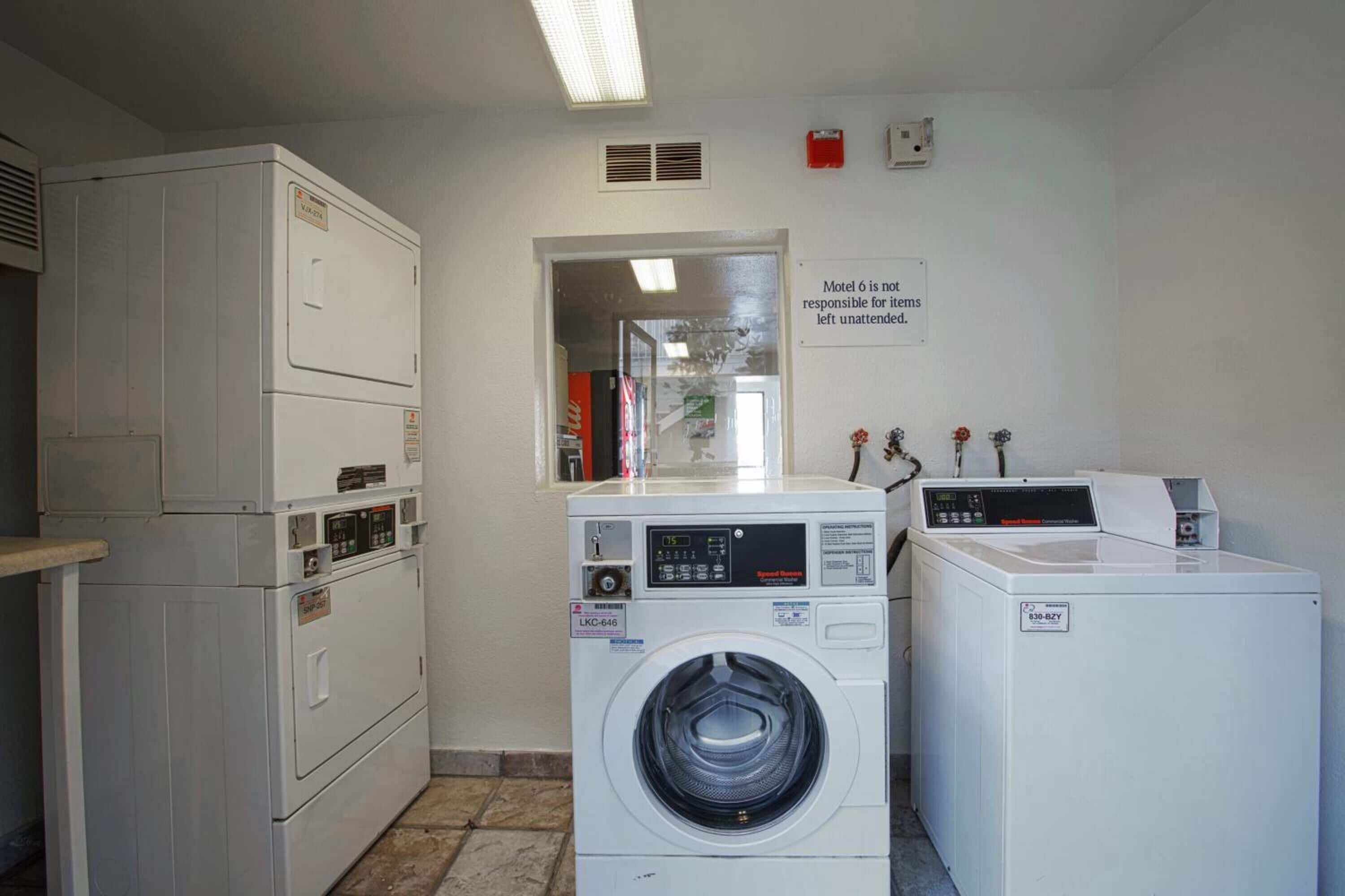 A laundry room with stacked washers and dryers, a vent on the wall, and a sign stating "Motel is not responsible for items left unattended."