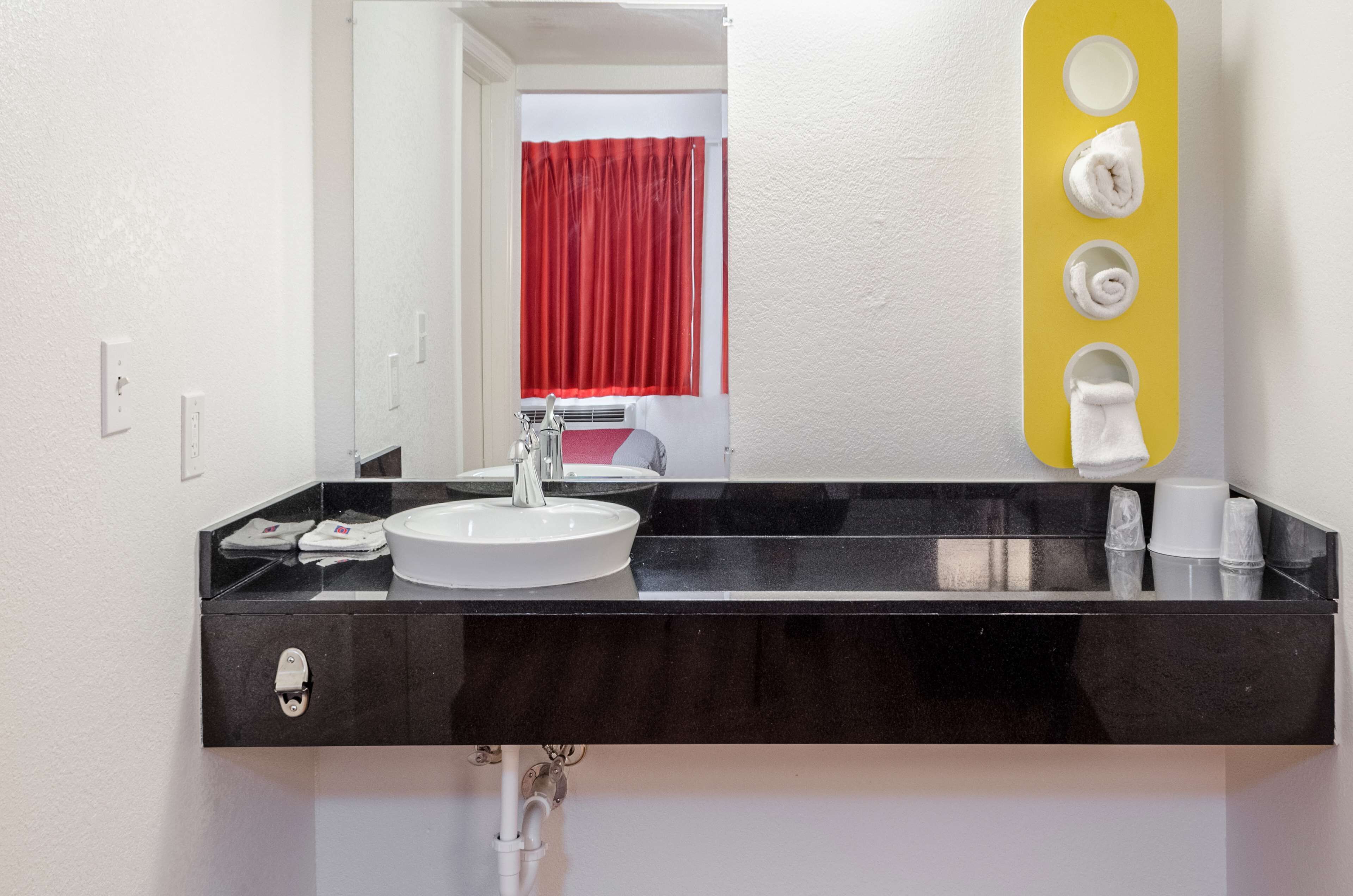 Casa de banho moderna com lavatório preto, torneira branca e espelho com suporte amarelo para toalha.