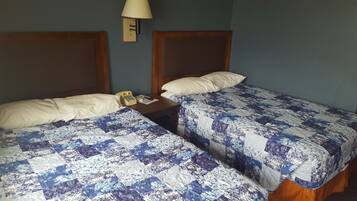 Una habitación de hotel con dos camas, cada una con una colcha de estampado floral, cabecero de madera y mesita de noche con teléfono y control remoto.
