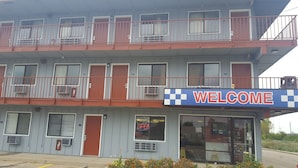 Ein zweistöckiges Motel mit einem 'WELCOME'-Schild, mehreren Balkonen und einem leuchtenden 'OPEN'-Neonzeichen.
