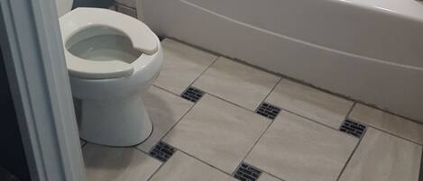 A bathroom with a bathtub, toilet, and tiled floor.