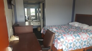 Ein Hotelzimmer mit Bett, Schreibtisch, Stuhl, kleinem Tisch, Spiegel und Fenster.