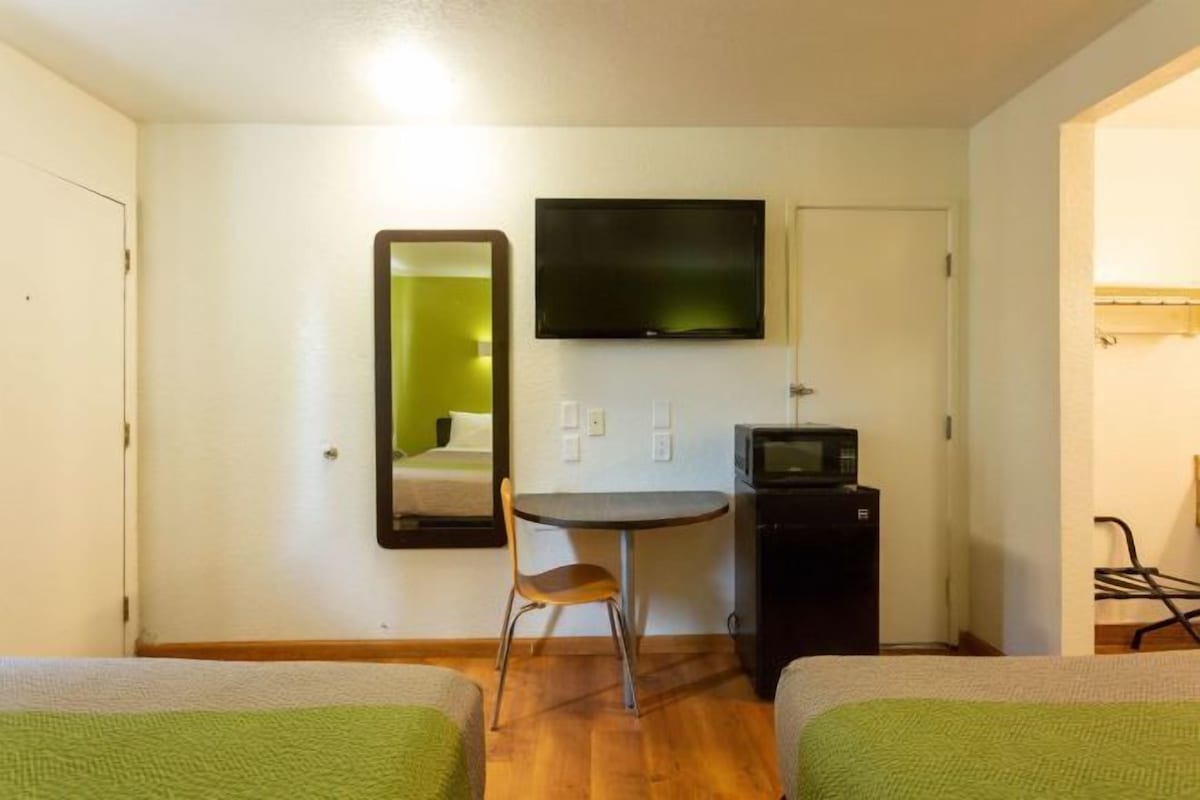 A hotel room with a bed, a desk with a chair, a television, and a microwave.