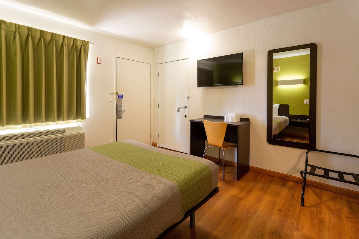 A hotel room with a bed, a desk, a chair, a TV, and a mirror.