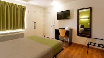 Una habitación de hotel con cama, escritorio, silla, televisión y espejo.