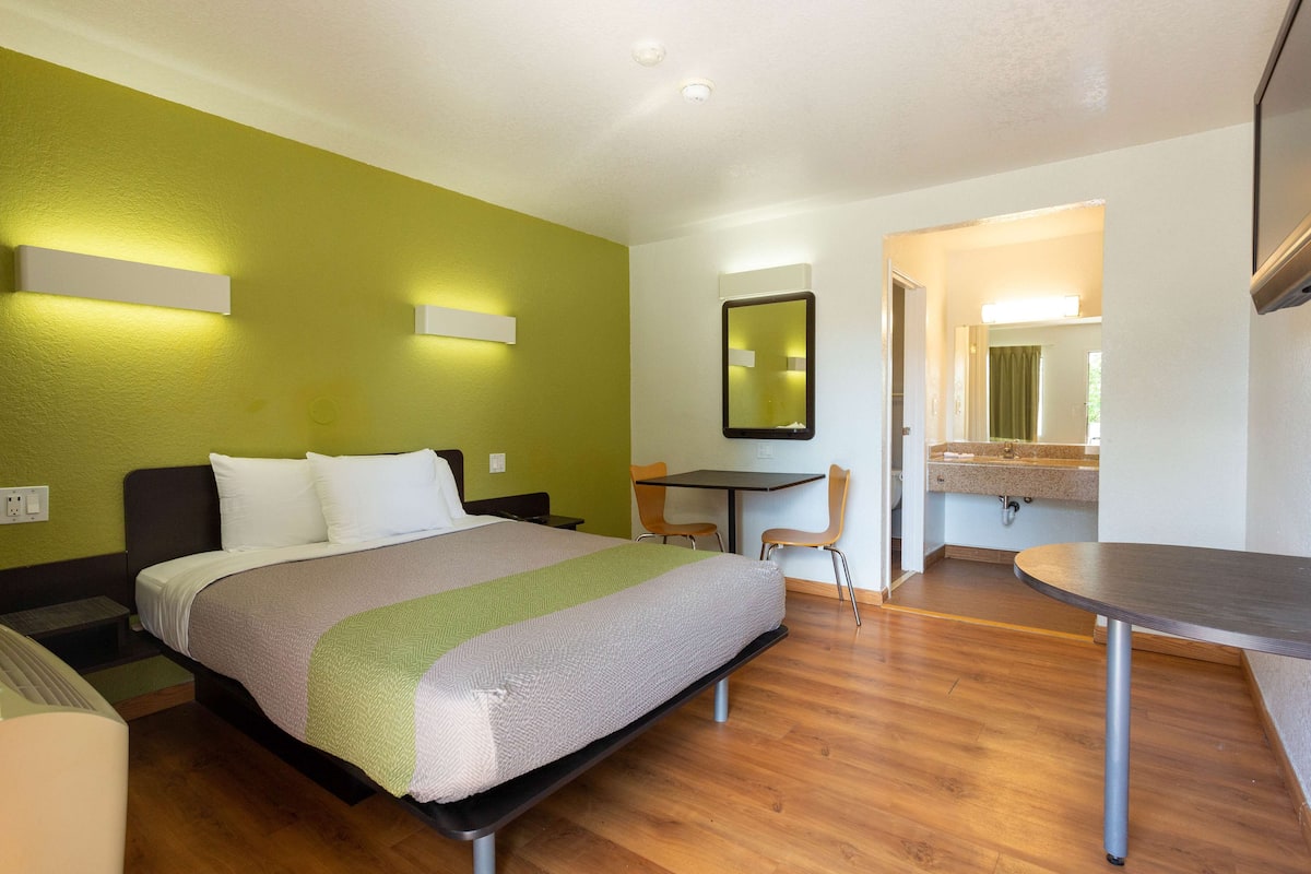 A hotel room with a bed, a desk, a chair, and a mirror.