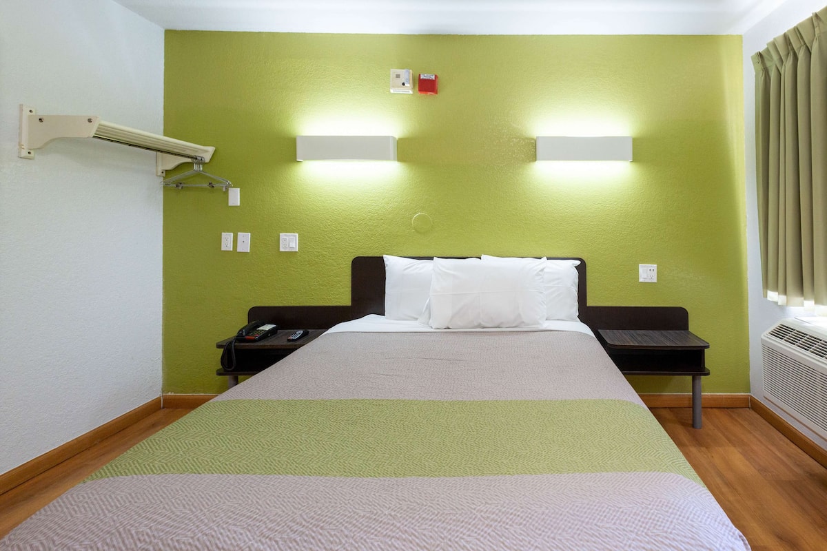 A hotel room with a bed, bedside tables, a wall-mounted light fixture, and a window with curtains.