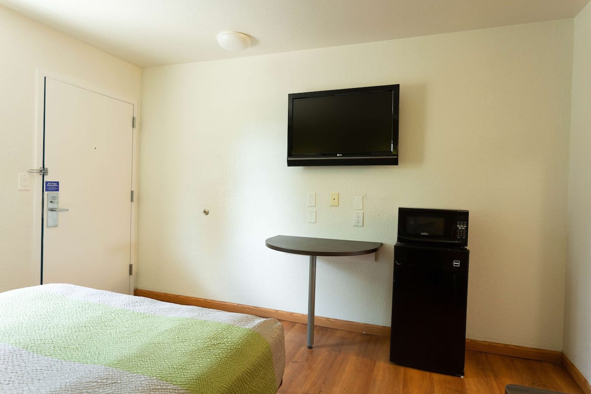 A hotel room with a bed, a television mounted on the wall, a small table, and a microwave.