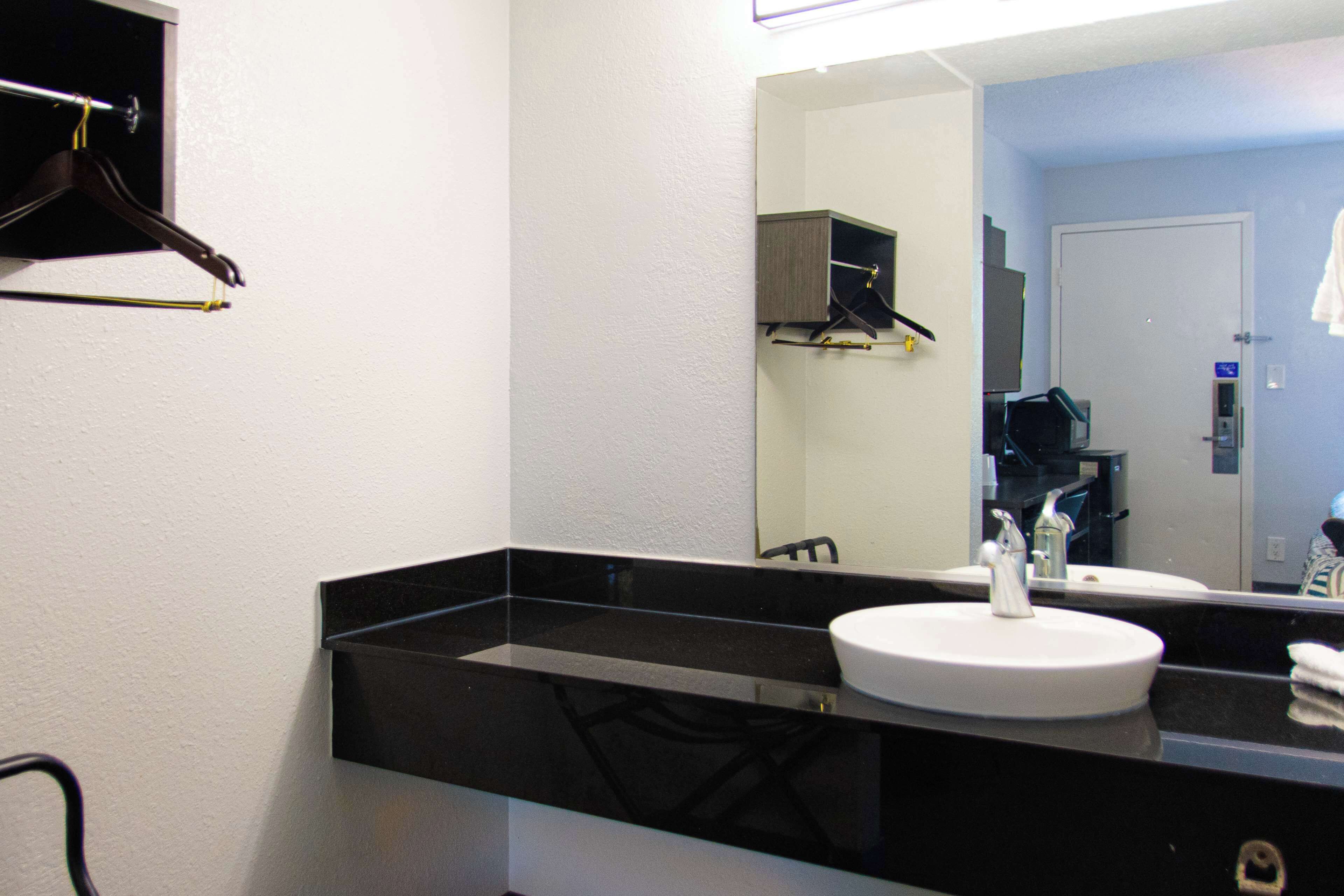A bathroom with a black countertop, a white sink, and a mirror. There is a towel rack and a door in the background.
