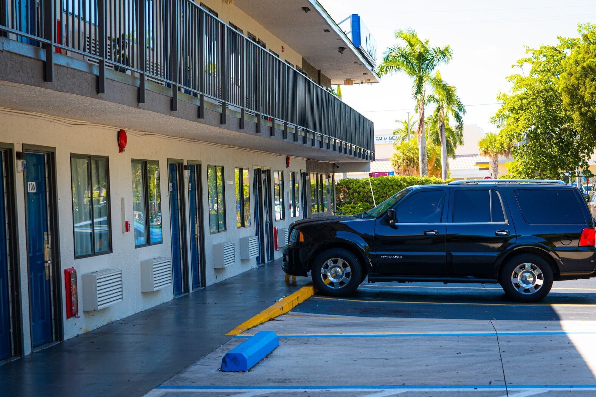 A black SUV parked in a parking lot with a building featuring multiple doors and windows in the background.
