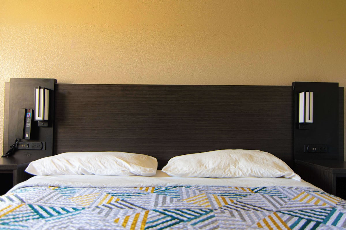 A hotel room with a dark wood headboard, white bedding, and a patterned bedspread.