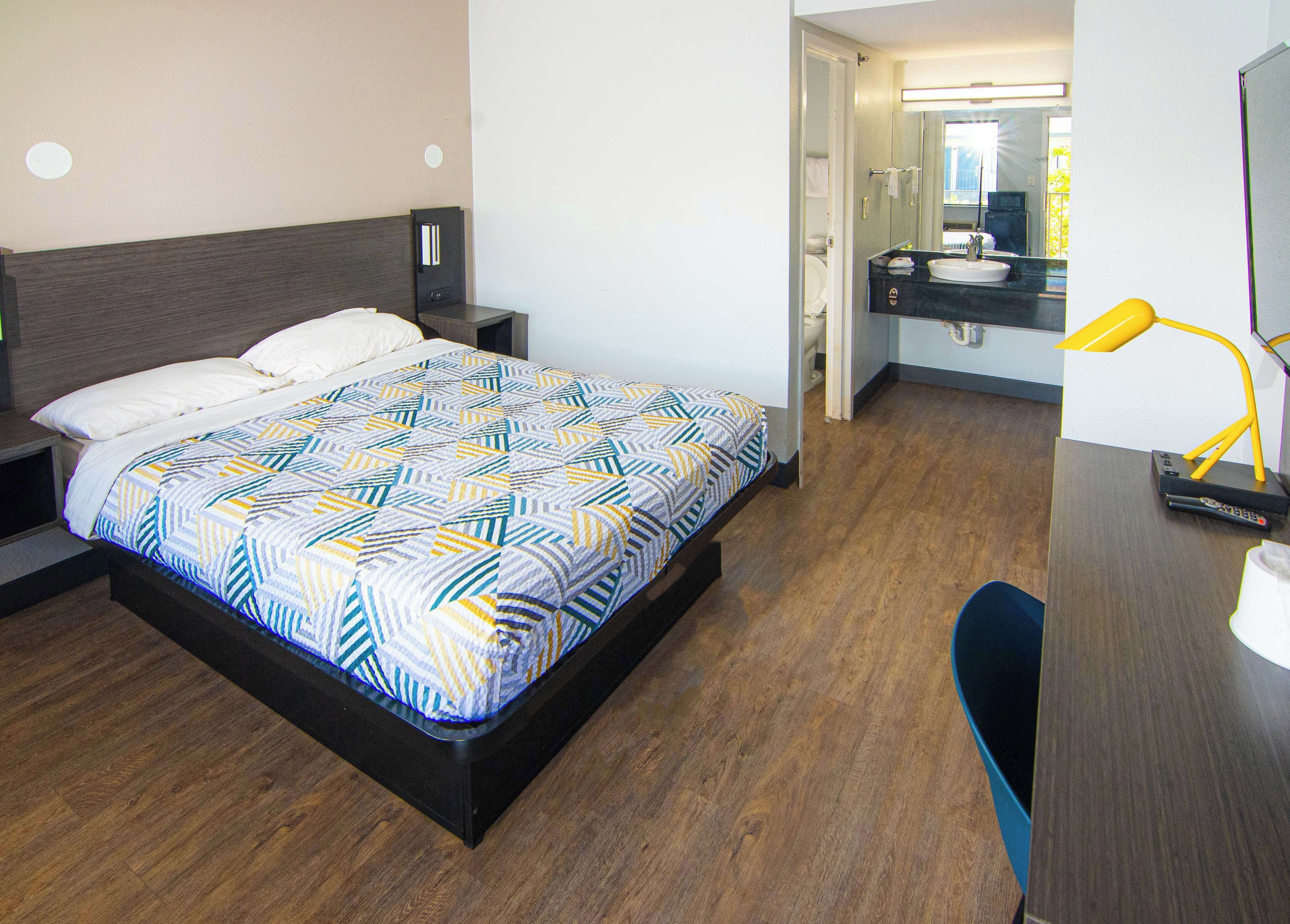 Una habitación de hotel con cama, mesita de noche y baño visible a través de una puerta abierta.