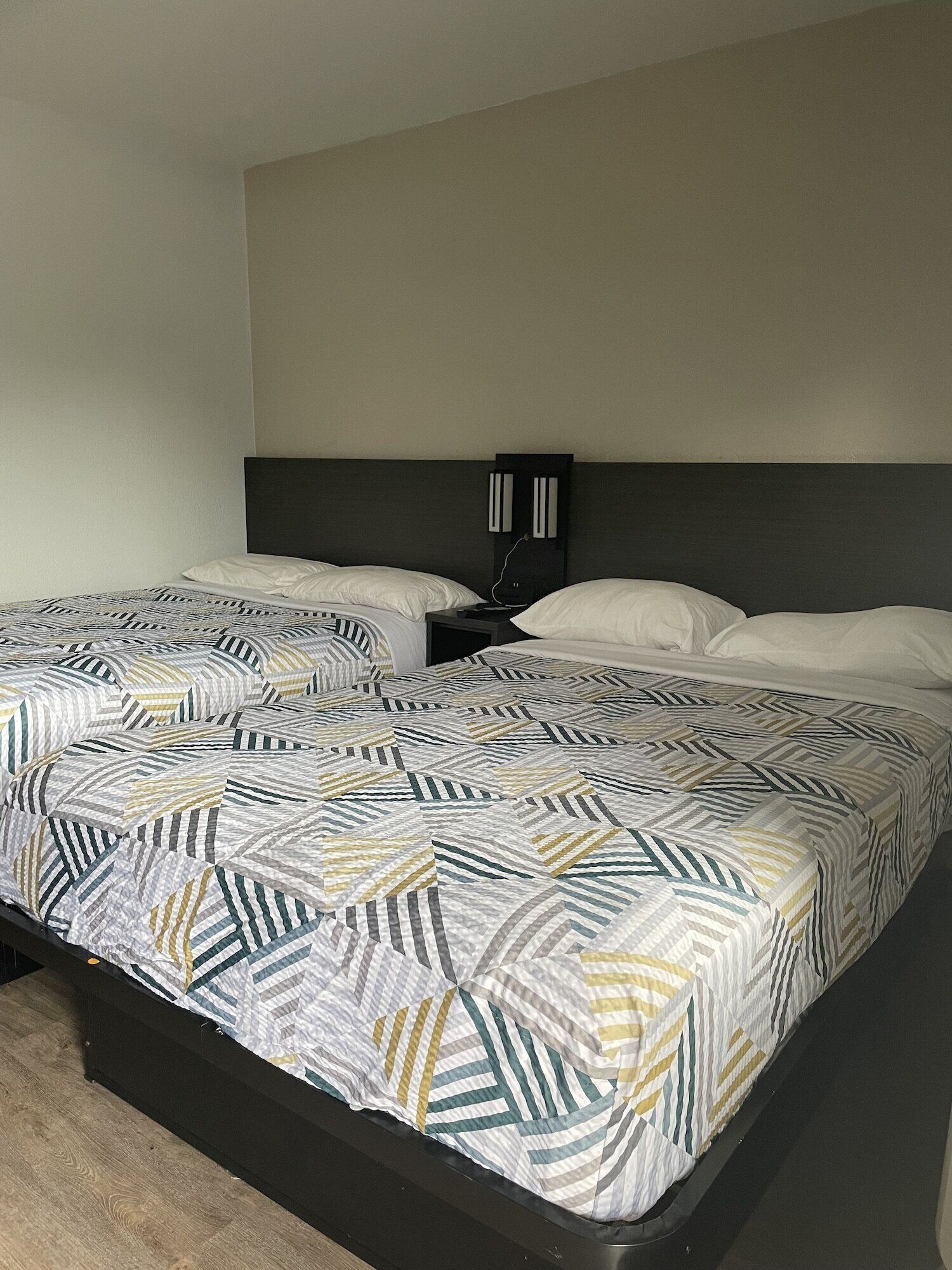 Una cama doble con un edredón estampado con motivos geométricos, un cabecero oscuro y una mesita de noche con una lámpara.
